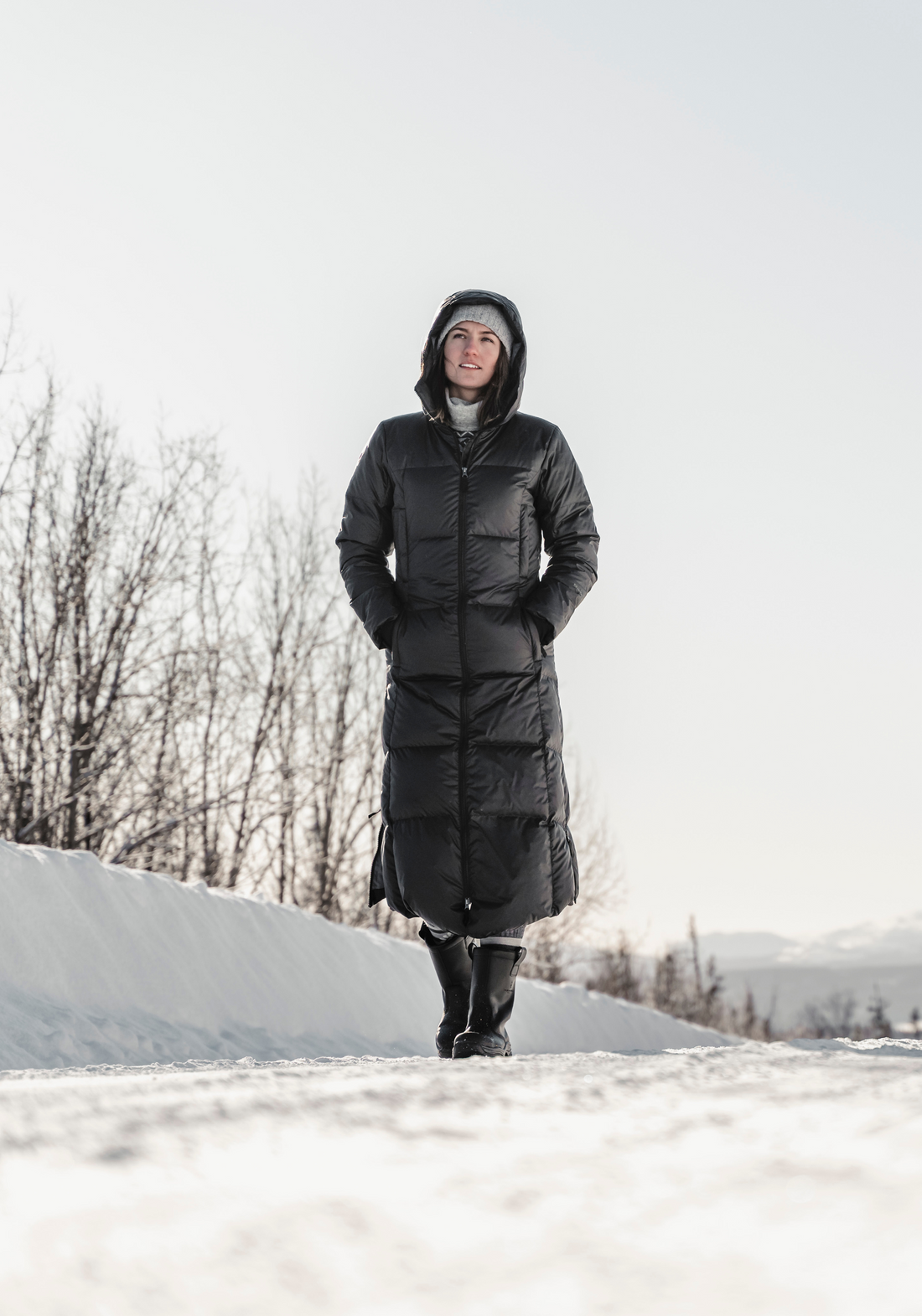 woman walking down a snowy street wearing long down hella coat from skhoop