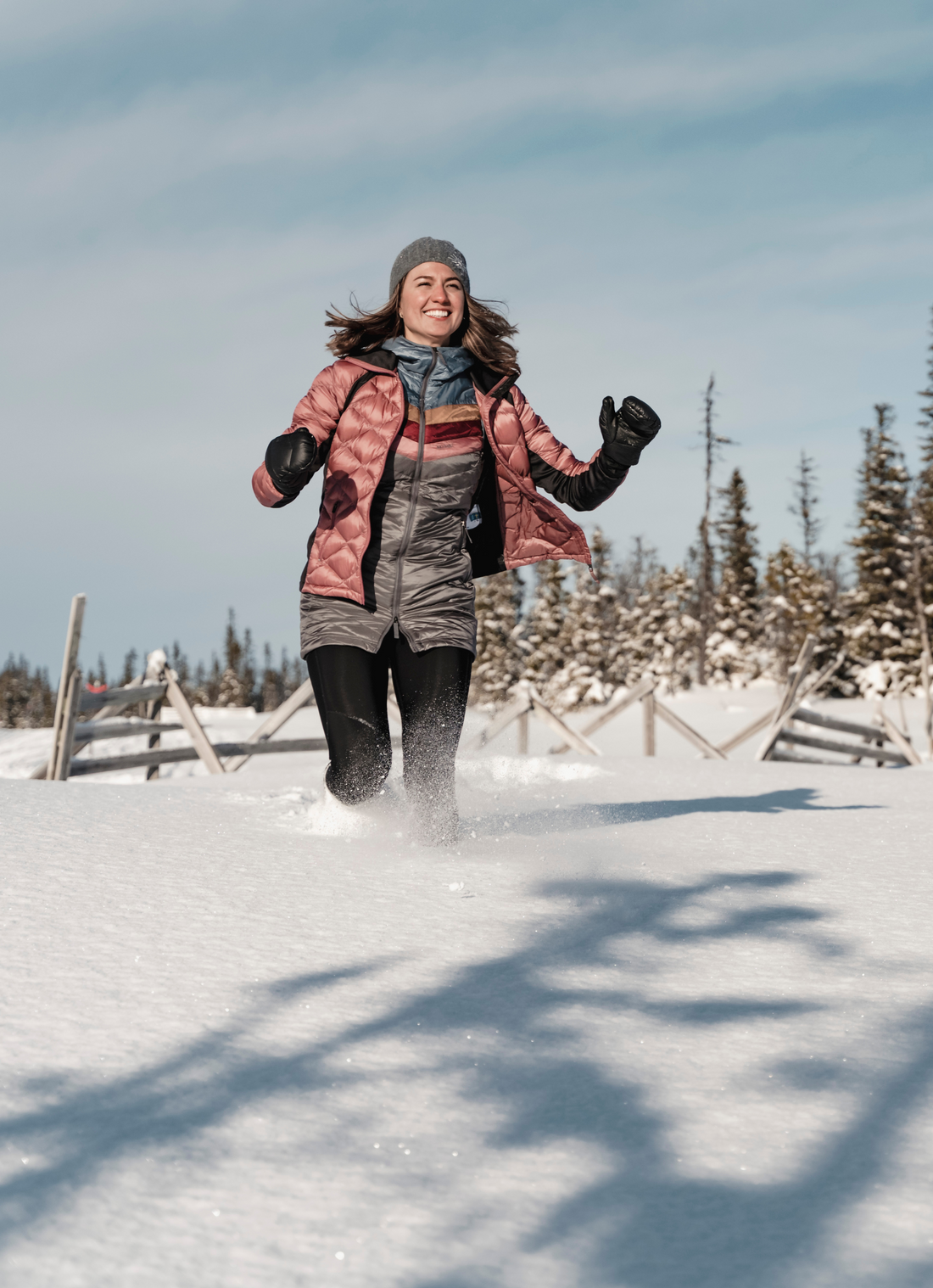 woman running through the deep snow wearing a puffy skhoop jacket and long vest