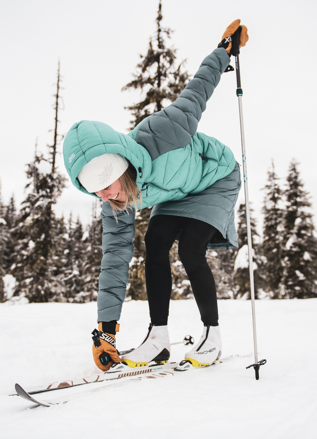 woman adjusting the bindings on her xc skis in skhoop klara jacket and short down skirt