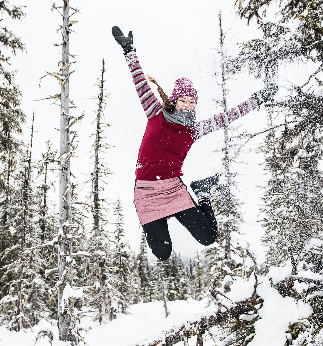 woman jumping off snowy log in pink skhoop kari skirt